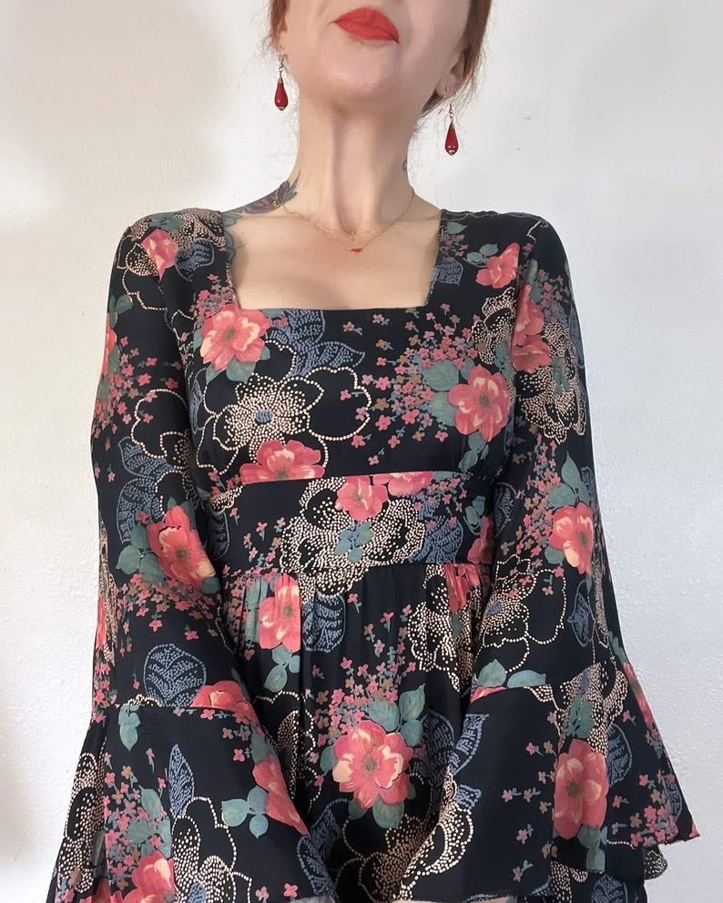 May include: A black maxi dress with a floral print featuring pink, red, and green flowers. The dress has a square neckline and long bell sleeves.
