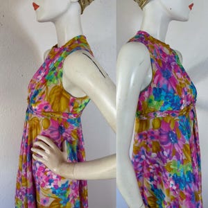 May include: A sleeveless floral print dress in shades of pink, blue, and yellow. The dress features a high neckline and a fitted waist. The fabric has a sheer quality, and the dress is displayed on a mannequin.