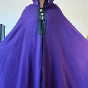 May include: A purple hooded cape with a black trim and a black lace-up closure at the neck.