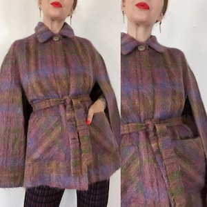 May include: A vintage cape coat in a plaid pattern, featuring shades of purple, green, and brown. The coat has a collar, a belted waist, and two front pockets. The fabric appears to be a soft, textured material.