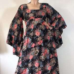 May include: A black maxi dress with a floral print featuring pink, red, and green flowers. The dress has long bell sleeves and a square neckline.