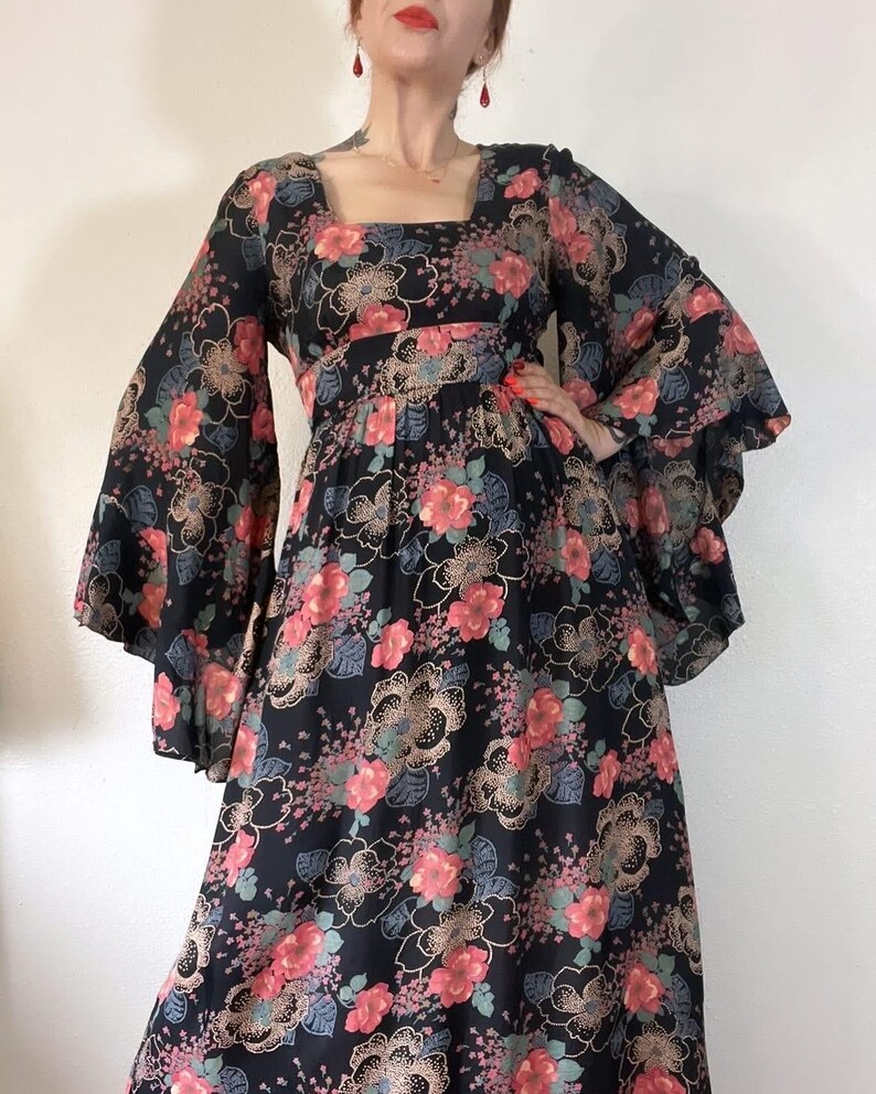 May include: A black maxi dress with a floral print featuring pink, red, and green flowers. The dress has long bell sleeves and a square neckline.