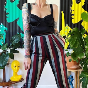 May include: A person wearing a black satin top with a sweetheart neckline and striped pants with black, red, and gray stripes.