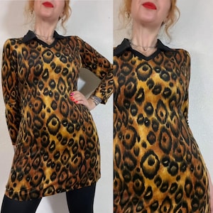 Puede incluir: Vestido de manga larga con estampado de leopardo, cuello negro y cuello en V. El vestido presenta un estampado de animales marrón y negro. La modelo lleva leggings negros. El vestido es de estilo vintage.