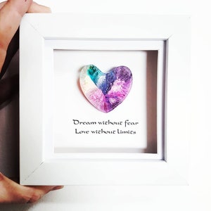 May include: A framed artwork with a heart-shaped design in teal, purple, and white hues. The white-framed piece includes the text "Dream without fear, Love without limits" in black script, set against a white background.