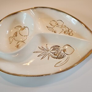 May include: A white ceramic serving dish with a gold rim and three sections. The dish is decorated with a gold pineapple, apples, and grapes.
