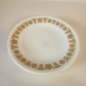 May include: White ceramic plates with a gold floral pattern around the rim. The plates have a simple, elegant design, perfect for everyday use or special occasions. The floral pattern adds a touch of vintage charm to the tableware.