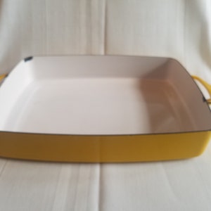 May include: A yellow enamel cast iron baking dish with white interior and two handles.