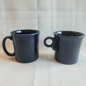 May include: Two blue ceramic mugs with a rounded shape and a single handle. The mugs are on a white surface.