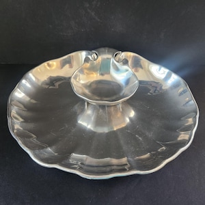 May include: A silver serving dish shaped like a seashell with a smaller bowl in the center. The dish has a scalloped edge and a shiny finish.