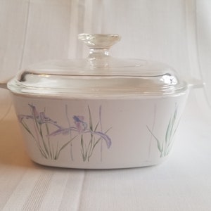 May include: White ceramic baking dish with a glass lid. The dish has a floral design with purple irises and green leaves.