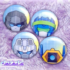 May include: Four circular pin-back buttons featuring stylized robot head illustrations. Each button displays a unique character with blue visor eyes against a light blue grid background. The designs include a grey, blue, white, and yellow robot.