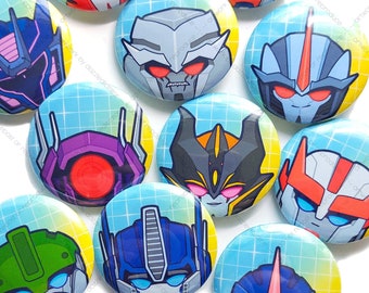 May include: A set of 12 round, colorful, cartoon-style character buttons featuring Transformers characters. The buttons are arranged in a grid pattern on a blue and white background. The characters include Optimus Prime, Bumblebee, Megatron, Starscream, and others.
