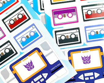Peut inclure: Un ensemble d'autocollants en forme de cassette audio colorés avec un logo Transformers et le texte "CASSETTE DAD". Les autocollants sont conçus pour ressembler à des cassettes audio vintage et présentent une variété de couleurs, notamment le rouge, le bleu, le jaune, le violet et le noir.