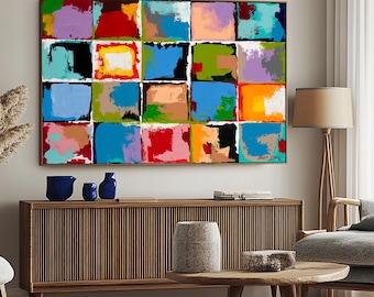 May include: Abstract painting with a grid of colorful squares in shades of red, blue, green, yellow, pink, and purple. The painting is framed and hanging on a wall above a wooden cabinet.