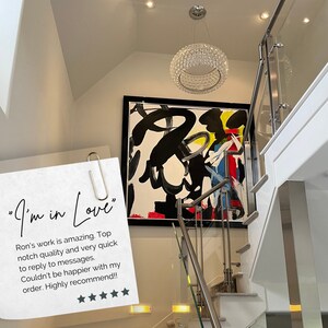 May include: A white wall with a black framed abstract painting featuring black, white, red, yellow, and blue paint strokes. A modern crystal chandelier hangs from the ceiling above the painting. A white staircase with a glass and metal railing is in the foreground. A handwritten note with the text "I'm in Love" and a review of the artwork is attached to the railing.