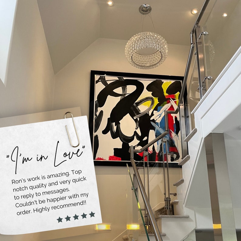 May include: A white wall with a black framed abstract painting featuring black, white, red, yellow, and blue paint strokes. A modern crystal chandelier hangs from the ceiling above the painting. A white staircase with a glass and metal railing is in the foreground. A handwritten note with the text "I'm in Love" and a review of the artwork is attached to the railing.
