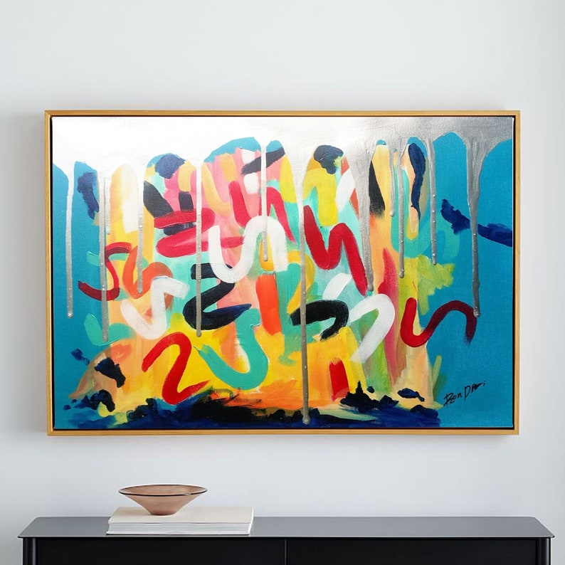 以下が含まれることがあります： 金色の額縁に入った抽象画。絵画は、カラフルな抽象的なデザインと、銀色の塗料の滴が特徴です。アーティストの署名「Ben Dan」は、右下の隅にあります。