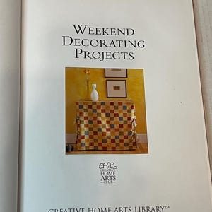 May include: A book titled "Weekend Decorating Projects" with a checkered fabric-covered table and a white vase with yellow flowers on top. The book is part of the Creative Home Arts Library.