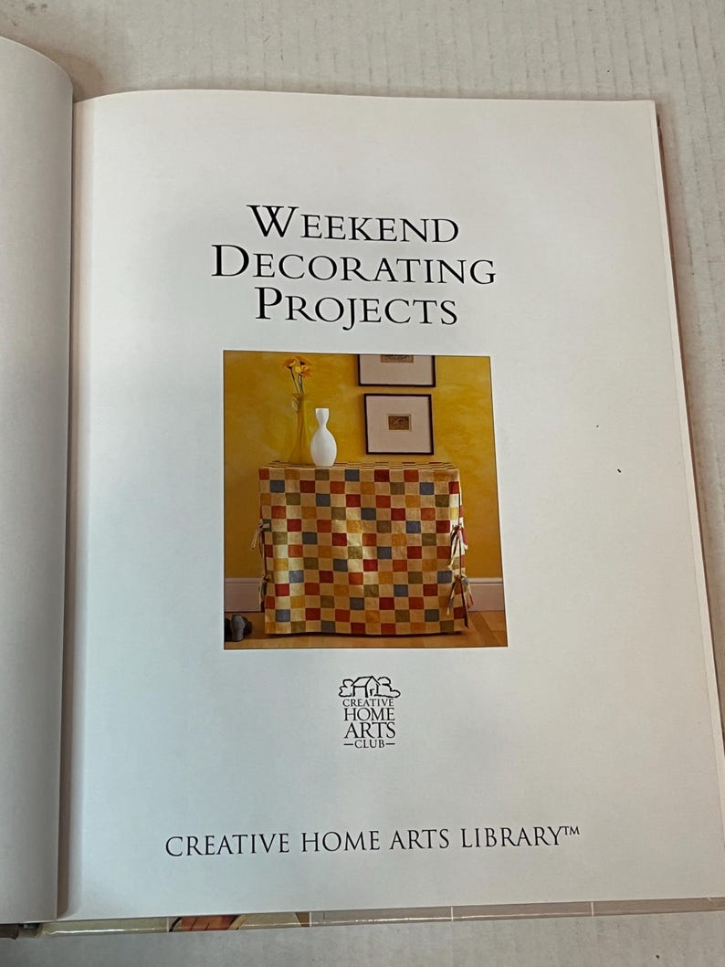 May include: A book titled "Weekend Decorating Projects" with a checkered fabric-covered table and a white vase with yellow flowers on top. The book is part of the Creative Home Arts Library.