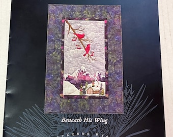 May include: A quilt pattern booklet titled A Journey to Light and Beneath His Wing by McKenna Ryan Pine Needles. The cover features a central image of two red cardinals on a branch above a snowy mountain cabin scene with purple borders.