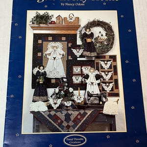 May include: A book cover titled "Angels In My Home" by Nancy Odom. The cover features a collage of angel-themed crafts, including dolls, quilts, and decorative items. The background is a dark blue with white stars.