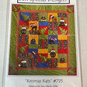 May include: A quilt pattern titled "Krismas Kats" by Sew Special Designs. The quilt design features black cats wearing Santa hats and Christmas trees on a patchwork background of red, green, blue, and yellow squares. The pattern is designed by Joni Pike.