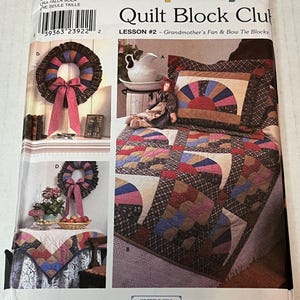 Könnte beinhalten: Simplicity Quilt Block Club Schnittmuster mit Lektion Nr. 2, Grandmother's Fan & Bow Tie Blocks. Das Cover zeigt einen Quilt mit Fächerdesign, einen Kranz mit rosa Schleife und eine Puppe. Das Muster wurde von Shirley Botsford entworfen.