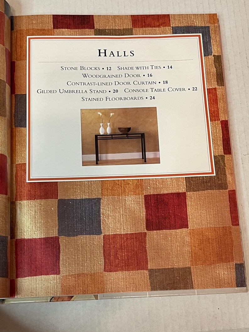 May include: A black metal console table with a wood-grain background. The table has a rectangular top and a lower shelf. The table is decorated with two small white vases and a bowl. The text "HALLS" is at the top of the image with a list of items and their prices.