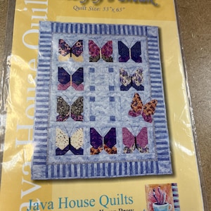 Pode incluir: Um padrão de colcha intitulado "Butterfly's Break" com um design azul e branco com motivos de borboletas. O tamanho da colcha é 135 cm x 165 cm. O pacote é da Java House Quilts, projetado por Karen Brow.