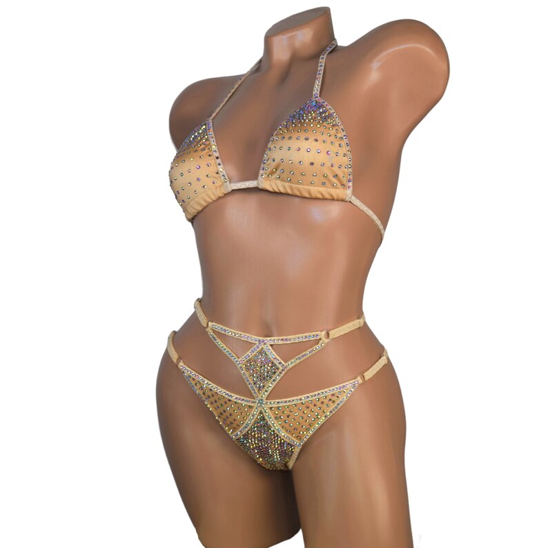 Puede incluir: Un bikini de color carne con un top halter y una parte de abajo de cintura alta. Ambas piezas est&aacute;n adornadas con pedrer&iacute;a iridiscente en un patr&oacute;n geom&eacute;trico.