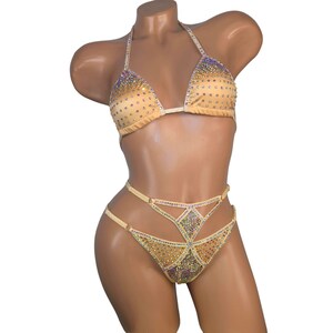 Puede incluir: Un bikini de color dorado con un top de halter y una parte inferior de corte alto. El bikini est&aacute; cubierto de pedrer&iacute;a iridiscente.