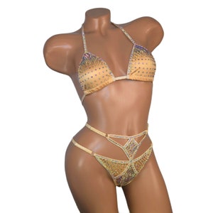 Puede incluir: Un bikini dorado con pedrer&iacute;a iridiscente. La parte superior es de estilo triangular con una tira halter. La parte inferior tiene una pierna de corte alto y un dise&ntilde;o cruzado en la parte delantera.
