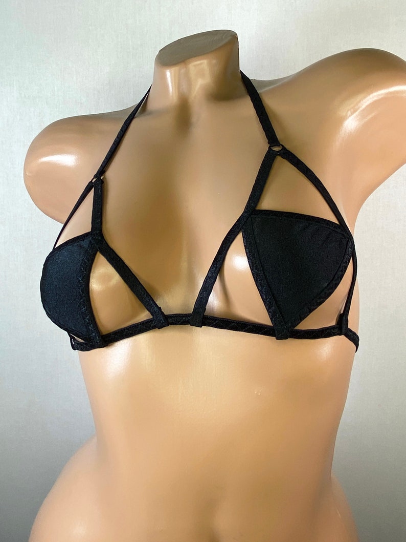 May include: Black lingerie top with a halter strap and a geometric design. The top has a triangle shape in the center and is made of a stretchy fabric.
