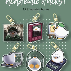 May include: Acrylic charms featuring cartoon ducks in various academic settings. Each charm is 1.75 inches and includes a gold-colored clasp. Designs include a duck in a beret painting, a duck as a book character, and a duck on a laptop with the text "hello bread".