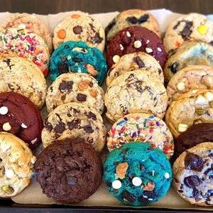 May include: A variety of cookies in a tray, including chocolate chip, red velvet, sprinkle, and peanut butter cookies.