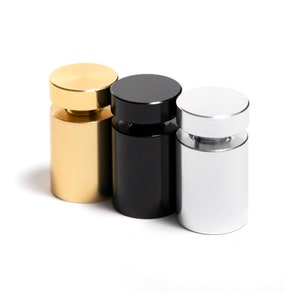 May include: Three cylindrical display stands in gold, black, and silver. The stands are made of metal and have a smooth, polished finish.