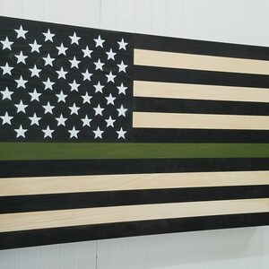 May include: A wooden American flag with a green stripe across the middle. The flag is painted black and white with a natural wood finish.