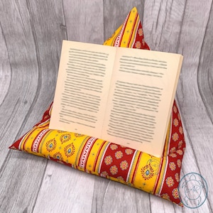 Könnte beinhalten: Ein gelber und roter Buchständer mit einem gestreiften und floralen Muster. Der Ständer hält ein Buch offen.