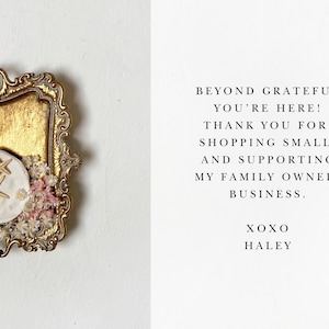 May include: A gold-colored tray with a white ceramic dish featuring two starfish. The tray is decorated with small white and pink flowers. The text on the right side of the image reads: "Beyond grateful you're here! Thank you for shopping small and supporting my family owned business. XOXO Haley."
