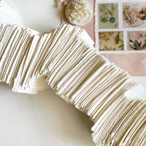 May include: A stack of white, handmade paper sheets with rough edges. The paper is arranged in a wave-like pattern.