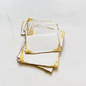 May include: A stack of white cards with gold foil edges. The cards are blank and ready for writing.