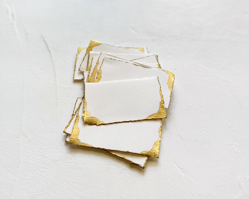 May include: A stack of white cards with gold foil edges. The cards are blank and ready for writing.