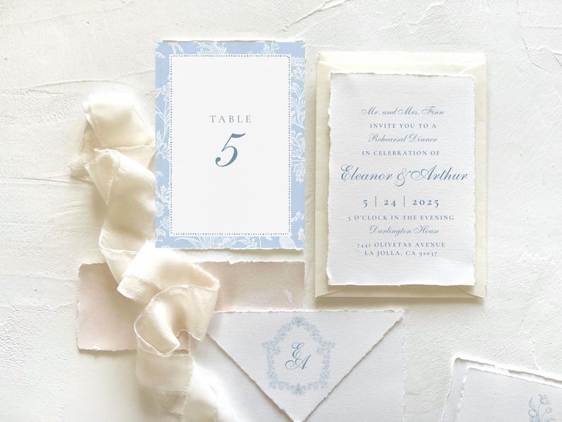 Pode incluir: Um convite de casamento azul e branco com um design floral. O convite inclui os nomes Eleanor e Arthur, a data 5.24.2025 e a hora 16h00. O convite tamb&eacute;m inclui a localiza&ccedil;&atilde;o, "Oliveta's Avenue, La Jolla, CA 92037".