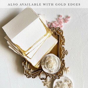 May include: A stack of white cards with gold edges on a gold tray. The tray is decorated with ornate details. The cards are blank and ready for writing.