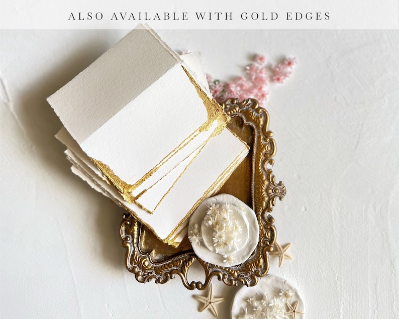 May include: A stack of white cards with gold edges on a gold tray. The tray is decorated with ornate details. The cards are blank and ready for writing.