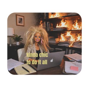 May include: A blonde doll with messy hair wearing a beige blazer sits at a desk with a laptop, a notebook, and papers. The text 'kinda chic to do it all' is overlaid on the image. Behind the doll, a bookshelf is engulfed in bright orange flames.