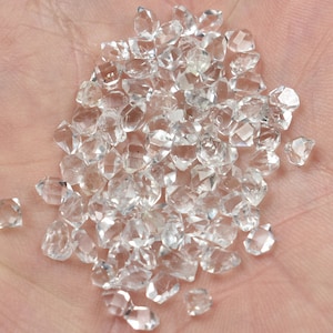 Peut inclure: Un tas de cristaux de quartz transparents et facetés, également appelés diamants de Herkimer, sur la main d'une personne.