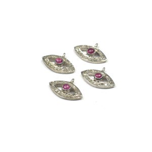Può includere: Quattro ciondoli argentati a forma di occhio con una piccola gemma rossa e rotonda al centro. I ciondoli sono circondati da piccole gemme trasparenti. Ognuno ha un piccolo anello nella parte superiore per il fissaggio a una catena o ad altri componenti di gioielleria.