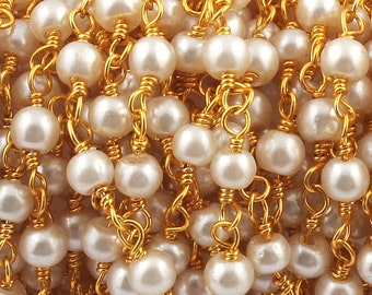 Op de afbeelding: Een close-up van een gouden ketting met witte parels. De ketting is gemaakt van kleine, delicate schakels en de parels zijn gelijkmatig verdeeld.